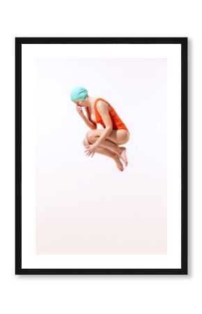 Portrait of young woman in swimming suit and cap jumping into water isolated over grey studio background. Dive-bombing