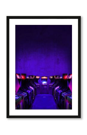 Old Unbranded Vintage Arcade Video Games in dark gaming room with purple light with glowing displays and concrete wall - vertical photo of retro design with free copy space for a poster or magazine