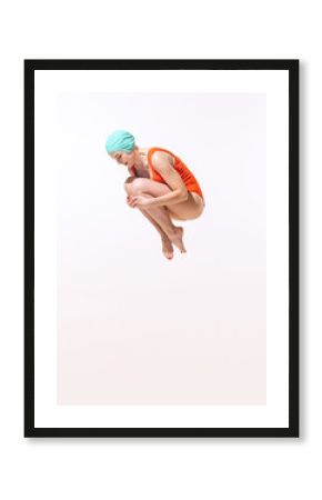 Portrait of young woman in swimming suit and cap jumping into water isolated over grey studio background. Dive-bombing