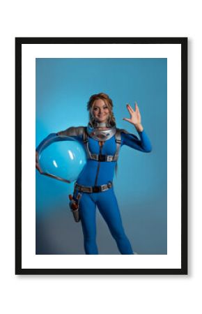Fantastic astronaut costume in retrofuturism style. A young beautiful blonde in a blue suit with a spherical helmet in her hands. pioneer of space exploration, atomic era, retro style