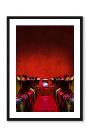 Old Unbranded Vintage Arcade Video Games in a dark gaming room with red light with glowing displays and concrete wall - vertical photo of retro design with free copy space for a poster or magazine