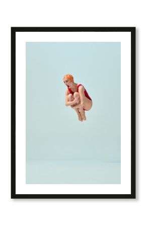 Diver in red vintage swimsuit and orange cap making cannonball pose in air with comic expression. Concept of summer fun, playful holiday, vintage swimsuit style, humor, retro sport.