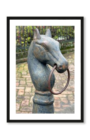 A vintage, metal, horse hitching post is shown in the Garden District of New Orleans, Louisiana during the day in a vertical view.