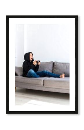 A boy sits on a gray couch, engrossed in a video game, a joyful expression on his face